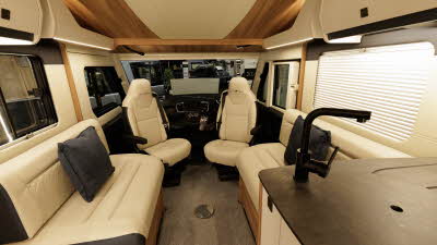 The Auto-Trail Grande Frontier GF-80 has cream leather upholstery with brown edging.  The front seats are swivelled to join the lounge.  There is a black cushion on each sofa.  The kitchen tap is to the bottom right and the sink has a cover.