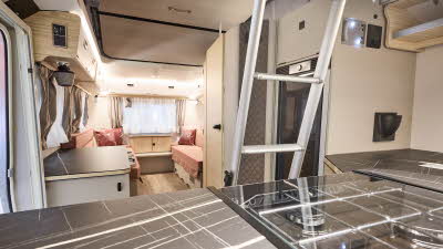 Interior of the Eriba Touring 620 Tango Red Edition with pink sofas, cosy red cushions, wooden accents and a wooden floor.  To the front is the kitchen and there’s a ladder to gain easy access to the pop top roof.
