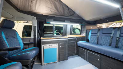 Vanworx Chesil’s interior has black leather upholstery with turquoise panels/pattern.  Its furniture is dark wood.  The three rear seats have seatbelts.  The roof is fully open revealing brown canvas.