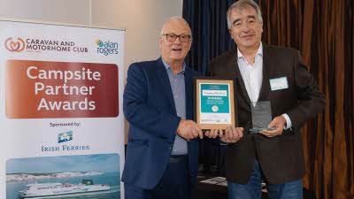 A Caravan and Motorhome Overseas Campsites Award Winner with the Chairman next to a sign showing Campsite Partner Awards, with Irish Ferries below it