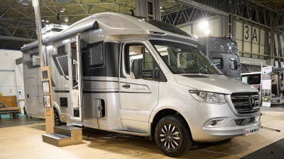 Adria Matrix Supreme's exterior is silver and black, the entrance door is open and there are wooden steps to gain easy access.  There is an interactive information board by the side of the van.