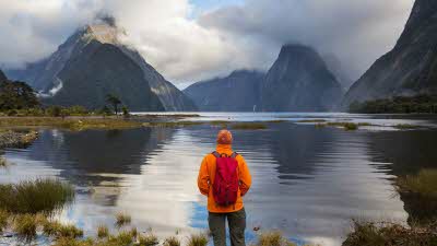 Looking over the calm water with high peaks disappearing into the misty clouds above at Milford Sound New Zealand