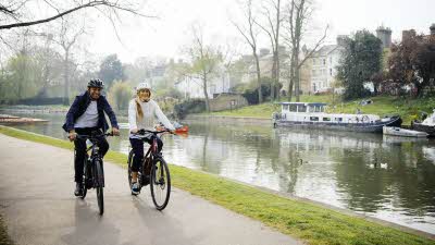 A couple riding e-bikes beside a canal with canal boat in the background