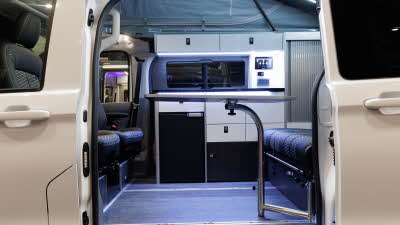 The Volksleisure Volkswagen Avoriaz T7 has black upholstery with white cabinets.  There is a table in front of the seats.
