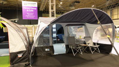 The Jamet Eco has a curved design.   There are two chairs in the awning.  The door to the trailer tent is open.