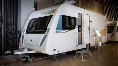 Xplore 554's exterior is white with turquoise and gold graphics, the door is open and there's a metal step for easy access into the interior.