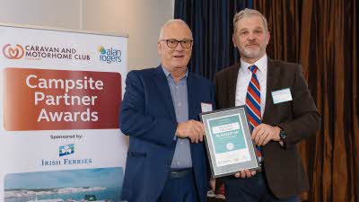 A Caravan and Motorhome Overseas Campsites Award Runner Up with the Chairman next to a sign showing Campsite Partner Awards, with Irish Ferries below it