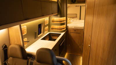 The Kaktus Adventure Vans Oasis has two tone brown upholstery with a wooden interior.  There is a fixed bed at the rear with a cupboard underneath.  The floor is wooden.