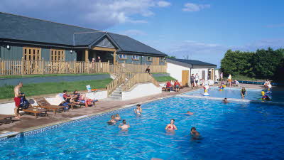 People in an outdoor swimming pool at Hillhead Caravan Club site on a sunny day