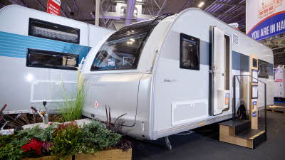 The Adria Altea 622 DP Dart’s exterior has light grey walls with a patterned decal from the front side window to the rear.  There are two wooden steps with an interactive display to the right. There is a floral display around its hitch