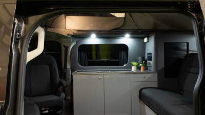 The AURA 4 Tend has black upholstery with matt grey walls and white cabinets.  There are two plants on the kitchen worksurface.
