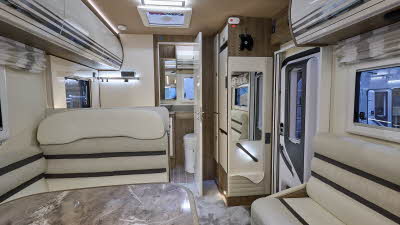 Roller Team Pegaso 590’s interior has cream upholstery.  Its furniture is cream.  At the rear there is a washroom.  There is a skylight above the central kitchen.
