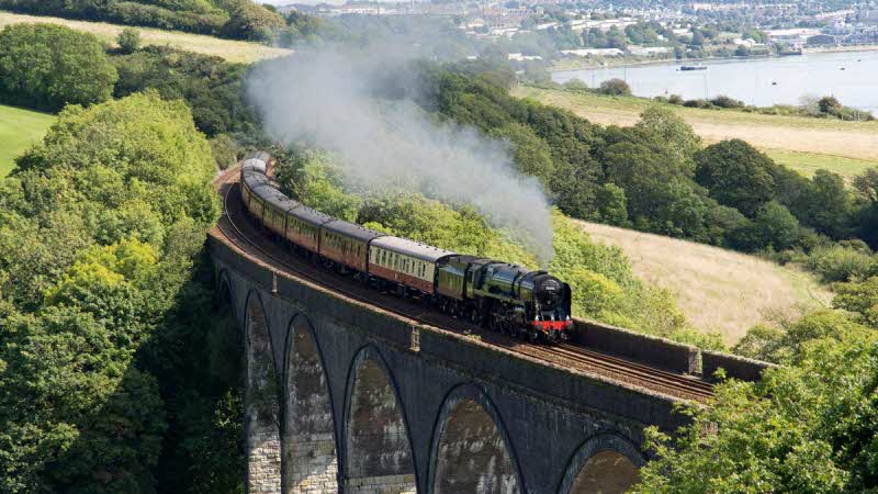 Steam train travelling at speed across Forder Viaduct, in Cornwall, UK