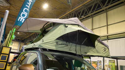 The Latitude Tents Pioneer has green canvas walls and a pale grey roof.  The window is open.  It has an extended platform with silver ladder to gain easy access