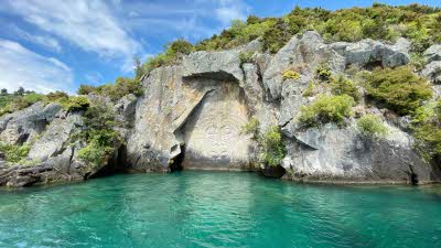 Turquoise water leading up to a rock face with carvings 