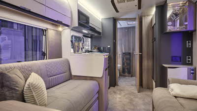 Swift Elegance Grande 835’s interior has wooden units with beige upholstery which has embossed patterns.  The rear door is open revealing the washroom