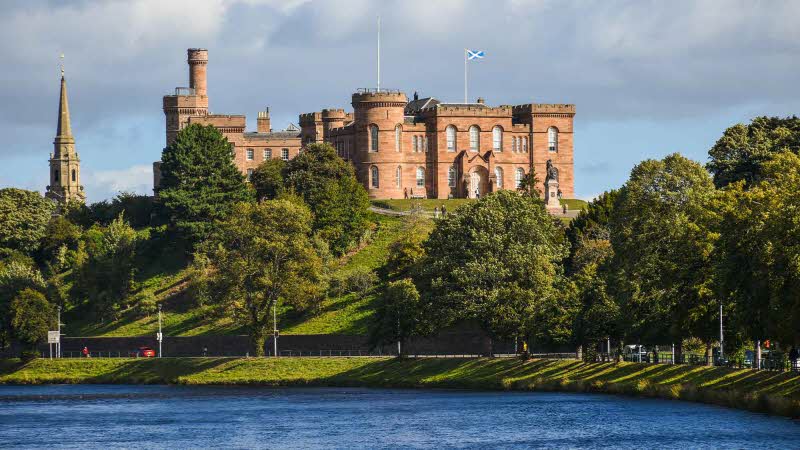 Inverness Castle in the distance rising above the trees in front which line the waters edge below