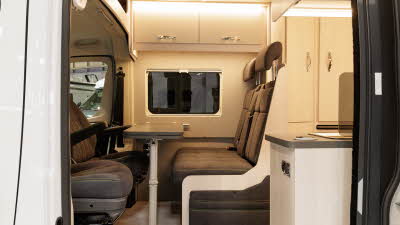 The Auto-Sleeper Active KB635 has brown upholstery with pale wood cabinets.  The front two seats are swivelled to join the dinette.