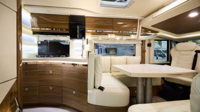 Eura Mobil Integra I 890 QB I’s interior has cream leather upholstery.  Its furniture is a dark wood with polished wooden doors.  The seating area around the table consists of a l-shaped sofa with a separate sofa and a front seat