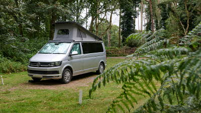 A campervan on an electric touring pitch in a leafy section of the campsite