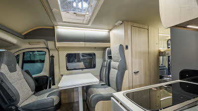 Auto-Trail Expedition 67 Flex's interior has two tone grey leather and beige fabric.  The furniture is wooden and the rear seats have fitted seatbelts.  There is a sky light above the dining table.  The kitchen sink and hob is to the right.