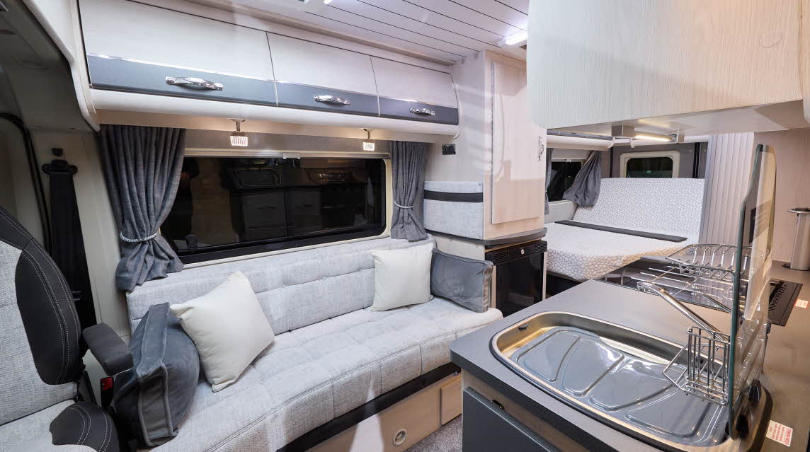 The Auto-Sleeper Kingham has grey carpet, with cream cabinets with grey highlights.  The upholstery is cream.  The arms of the driver’s seat are grey and there are cream and grey cushions.  There is a fixed rear bed.