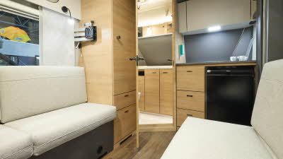 Knaus Yaseo 340PX’s interior has wooden furniture and its upholstery is cream.  There is a kitchen and washroom to the front of the caravan.  There is a black fridge in a unit.