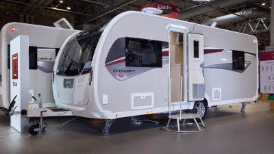 Elddis Crusader Aurora’s exterior is grey with a grey and dark red patterned decal.  The entrance door is open and there is a large metal step to gain easy access.  The roof light is open and there is a TV aerial on the roof.