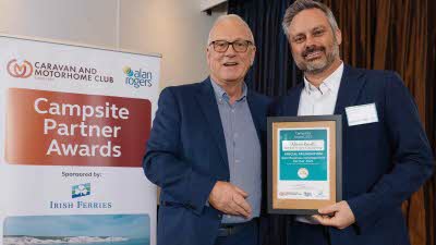 A Caravan and Motorhome Overseas Campsites Award Winner with the Chairman next to a sign showing Campsite Partner Awards, with Irish Ferries below it