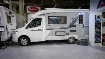 Auto-Sleeper Bourton's exterior has a white cab and grey body with grey/blue decals.  The entrance door is closed and there is a step to gain easy access.