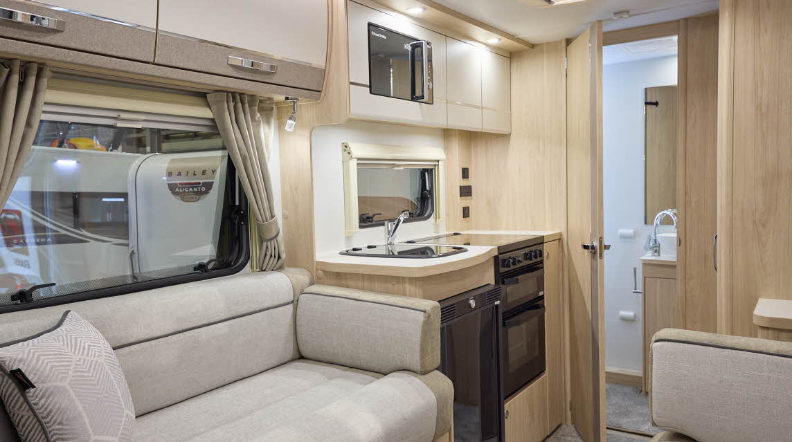 The Elddis Accordo 105 has a beige carpet, with cream and pale brown cabinets.  The upholstery is cream and pale brown with dark brown piping.  Through the opened interior door is a rear washroom.