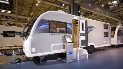 The Bailey Pegasus Black Amalfi has a grey exterior with a grey decal including pale blue ripples on it,  The front door is open and there is an interactive stand next to the two metal steps.