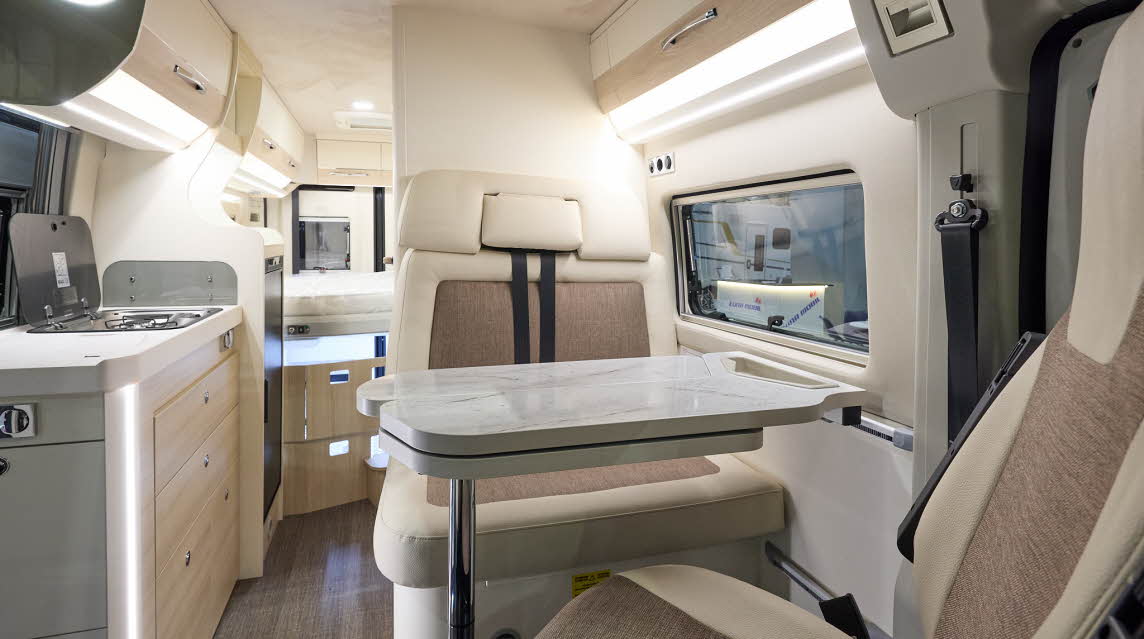 Eura Mobil Van 635 has wooden flooring with mid brown and cream upholstery.  The cabinets are cream and pale wood.  There is a step to reach the fixed rear bed.