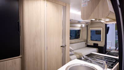 The Elddis Autoquest CV20 has cream and pale brown cabinets.  The upholstery is cream and pale brown with dark brown piping.  The round sink is in the front.  There is a rear lounge with two sofas. One of the rear doors is open.