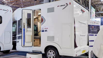 Auto-Trail F-Line F60 exterior, the motorhome is white, the habitation door is open showing into the interior, with a step to gain easy access.  There is a blue Auto-Trail umbrella in the door.