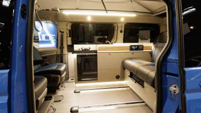 The Hillside Leisure MVX has black and blue upholstery, its cabinets are pale wood.  The fridge is black. 