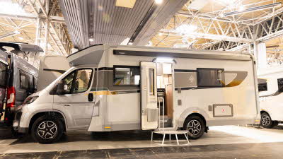 The Buccaneer Quantum F-4S has a silver cab with a white coachbuilt body.  It is decorated with decals of various colours.  Its habitation door is open and there is step to gain easy access.