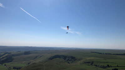 A solo paraglider floating in clear skies over the Peak District