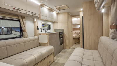 Interior of the Elddis Whirlwind Evolve 868 with cream sofas and wood accents and beige carpets.  The door to the rear bedroom is open.  Perfect for relaxation and designed for comfort.