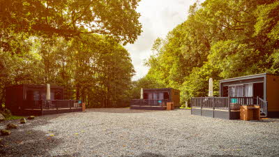 Three glamping pods on gravel area under green trees