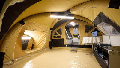 The Raclet Sequoia GL has a dark cream coloured canvas.  The bedroom door is open.  There is a step to the bedrooms.  The kitchen unit is in the front of the photo.  There is a strip light on the air beams.