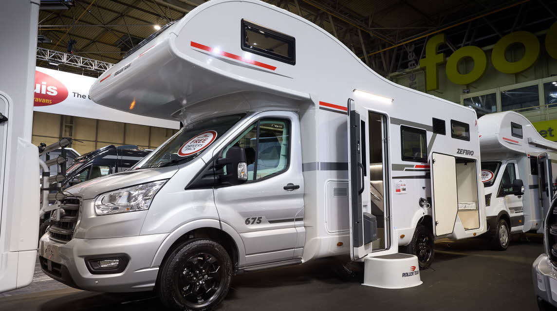 The Roller Team Zefiro 675 has a silver cab and its body is white with grey and red decals.  There is a white step outside the open habitation door.  The rear locker door is open.