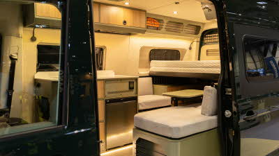 The Onyx Vans Summit 2.0 has cream upholstery with wooden cabinets.  The table and cupboard exteriors are pale green.  To the rear there is a fixed bed.