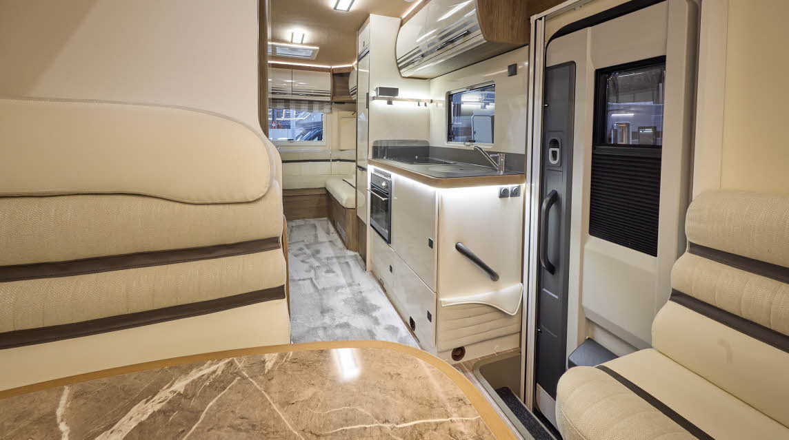 The Roller Team Pegaso 745 has grey carpet.  The upholstery is cream leather with dark brown highlights.  There is a marble effect table in front of the sofas.  The cabinets are cream with wooden surrounds.  There are two skylights.