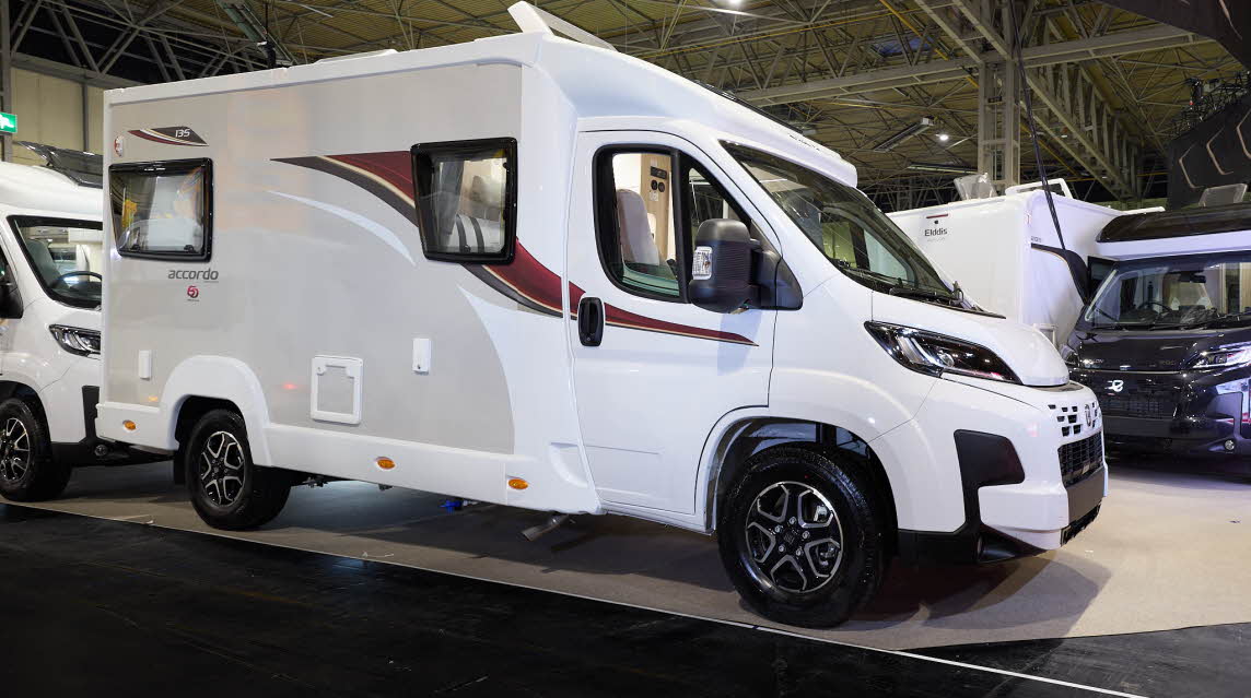 The Elddis Accordo 135 has a white body with a grey side panel.  There are red and black decals.  Its skylight is open.