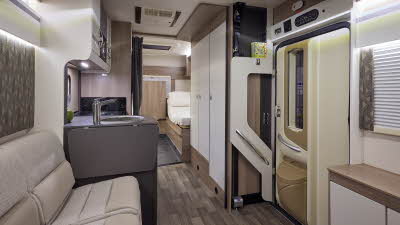 The Coachbuilt GB LIV Swift Escape 674 has a wooden floor, with cream cabinets. The upholstery is cream and light brown. There is fixed rear bed, close to the en suite washroom.