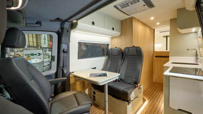 Project Yonder Freedom's interior has black upholstery.  The furniture is white with pale green doors.  At the rear there is a fixed bed.