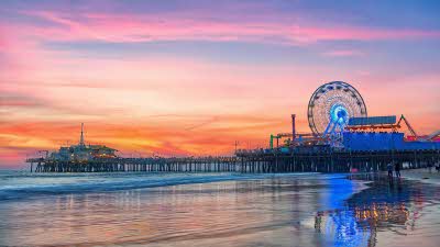 The big wheel rising high with the pier extending out in front over the calm waters under the sunset sky of pink and orange