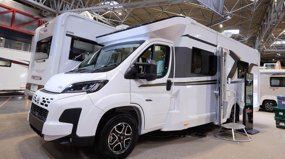 The Elddis Avalon 285 has a white body with black and gold decals.  There is a metal step by the open habitation door, there is an interactive stand to the right.
