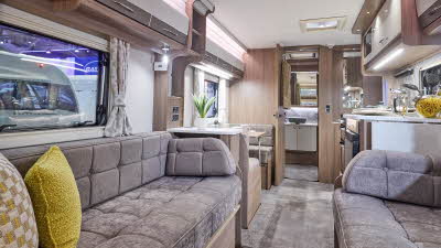 Interior of the Coachman VIP 520 with dark grey sofas, cosy cushions and wood accents and large windows and two skylights.  The door to the rear washroom is open.  Perfect for relaxation and designed for comfort.